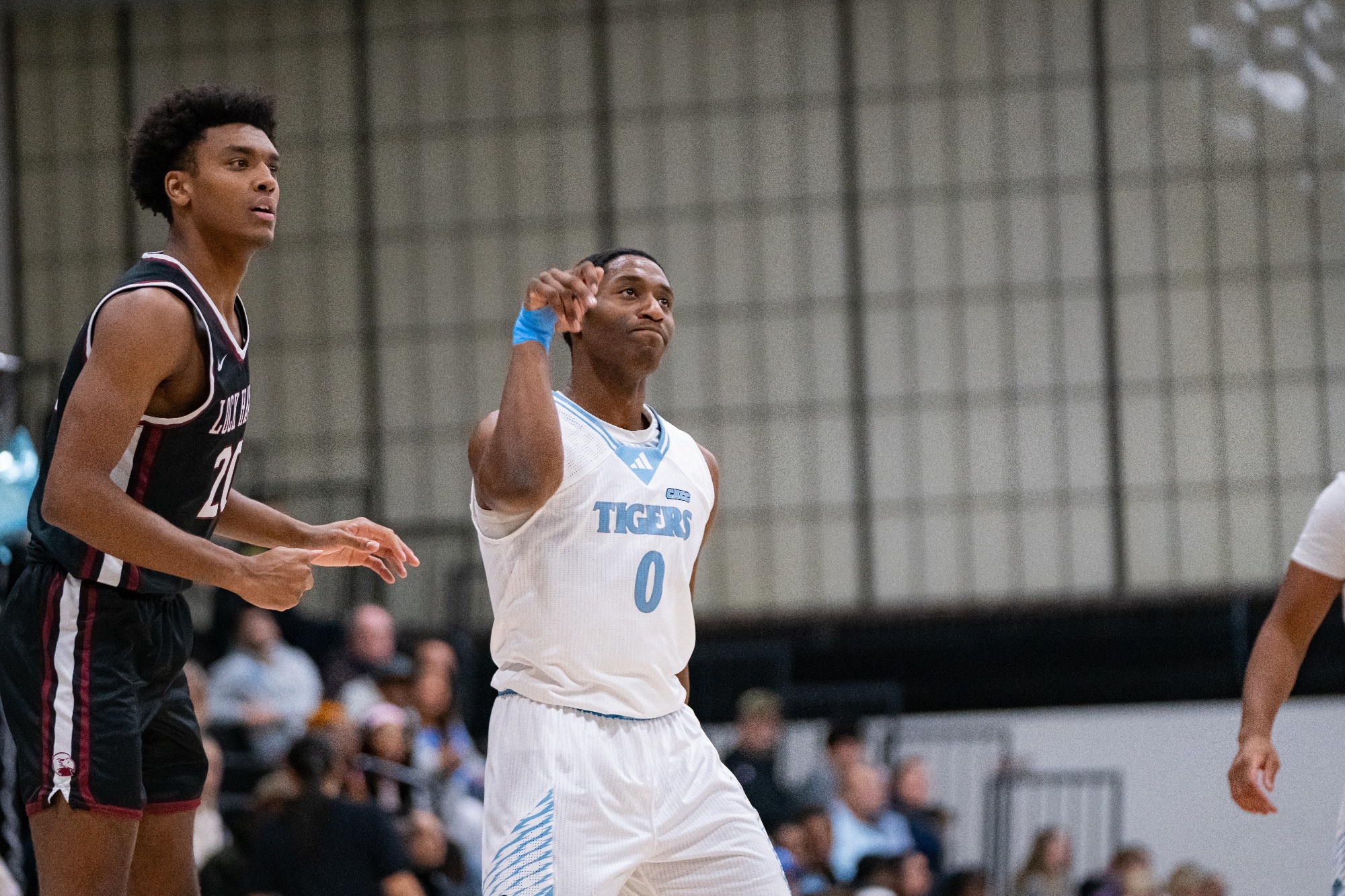 RJ Delahaye after shooting a basketball, with his arm raised and wrist curled as a defender from his right looks on