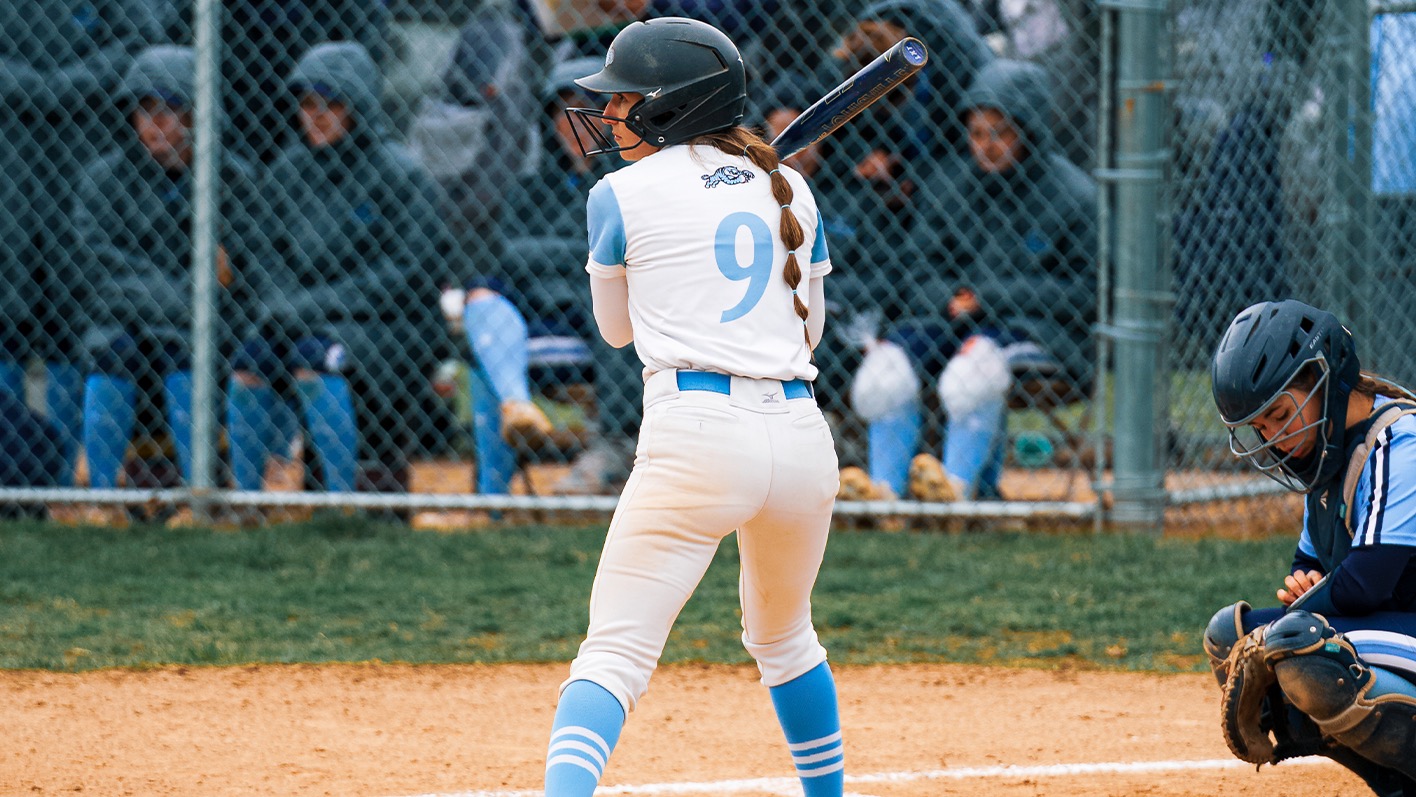 A closeup of Rylee Hobel, I the right-handed batter's bx, from behind as she prepares for a pitch to be thrown