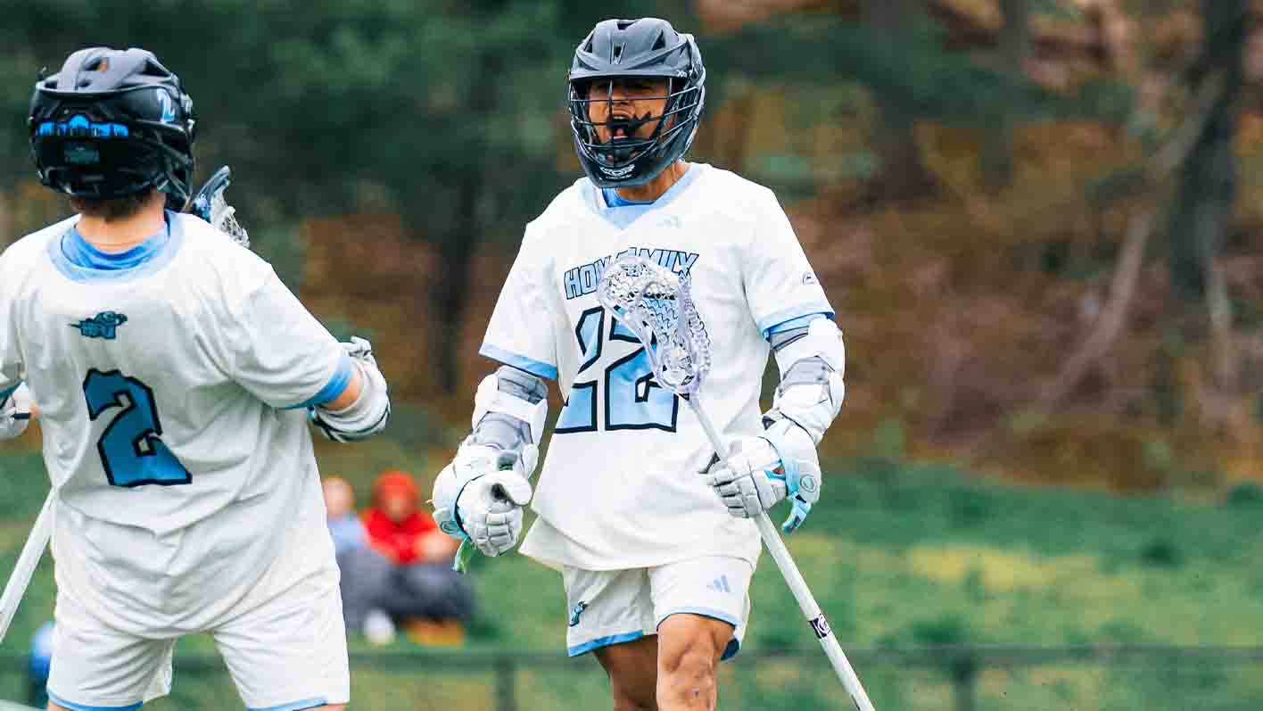 A closeup of Jayden Williams celebrating with a teammate,  yelling while holding his stick in his left hand