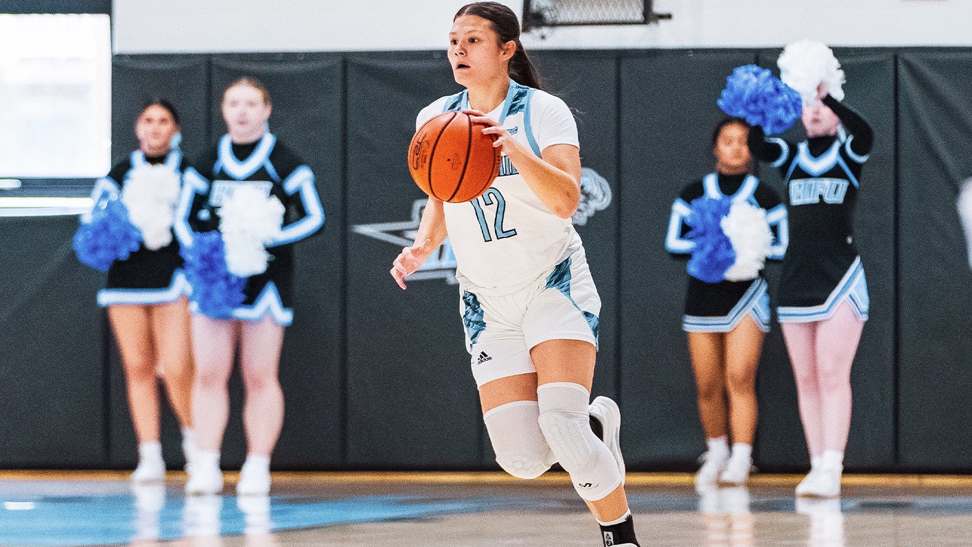 Amy Ngo dribbling with her left hand, a group of four HFU cheerleaders in the background behind her