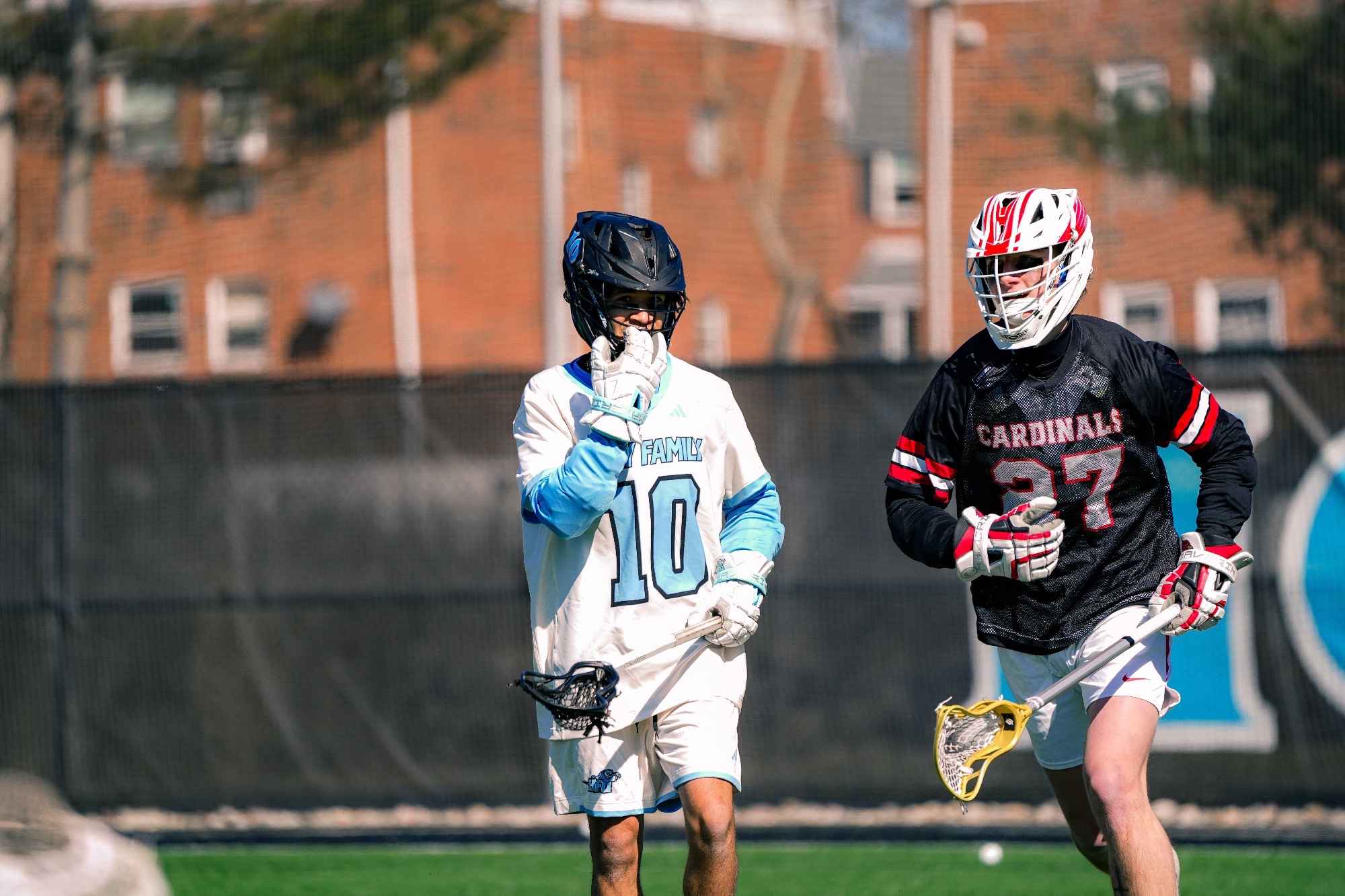 A closeup of Jaelin Benson, who is touching his face mask with his right hand while holding his stick with his left next to a defender