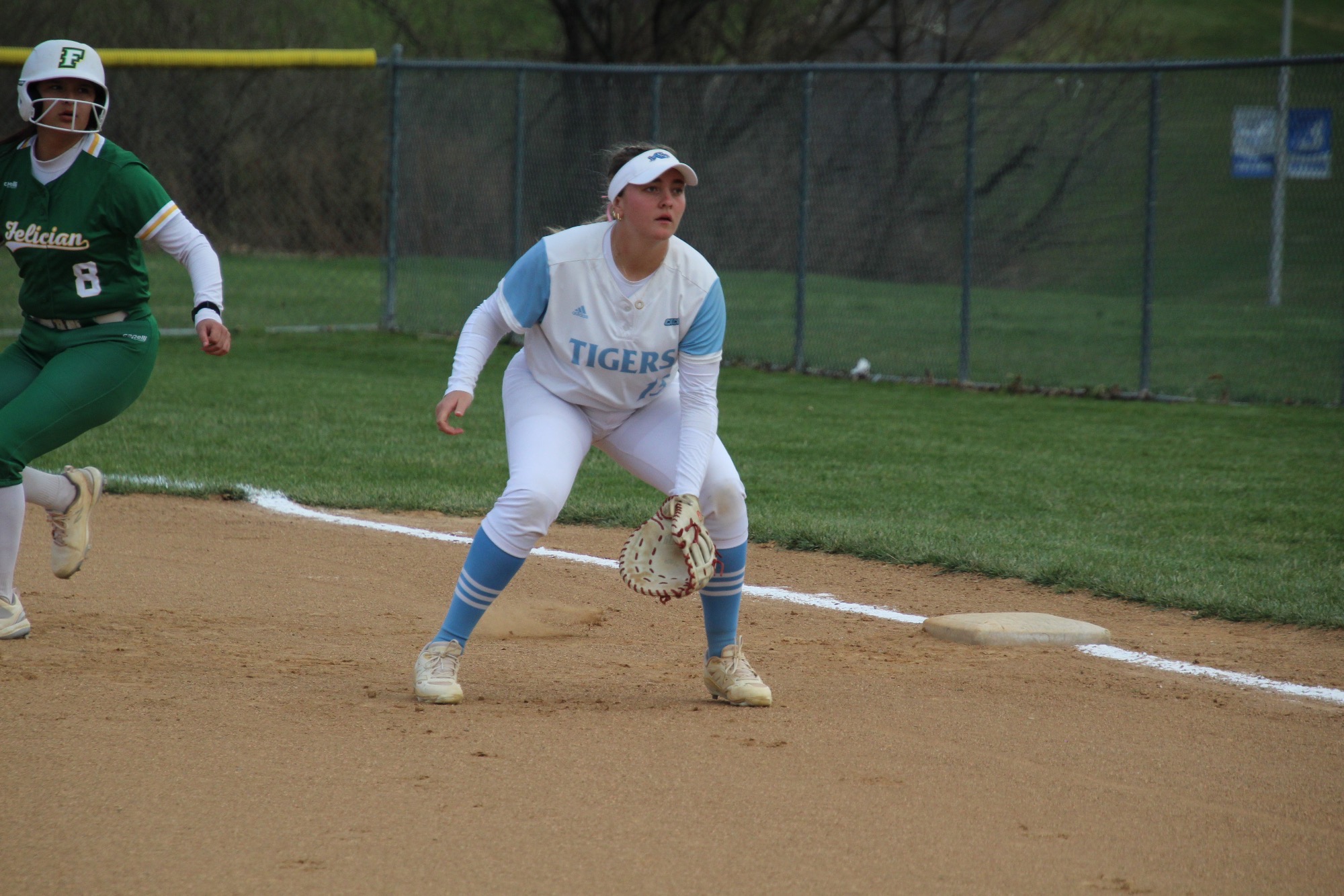 First baseman Olivia Croge enters a ready position, an opponent behind her taking a lead off first base