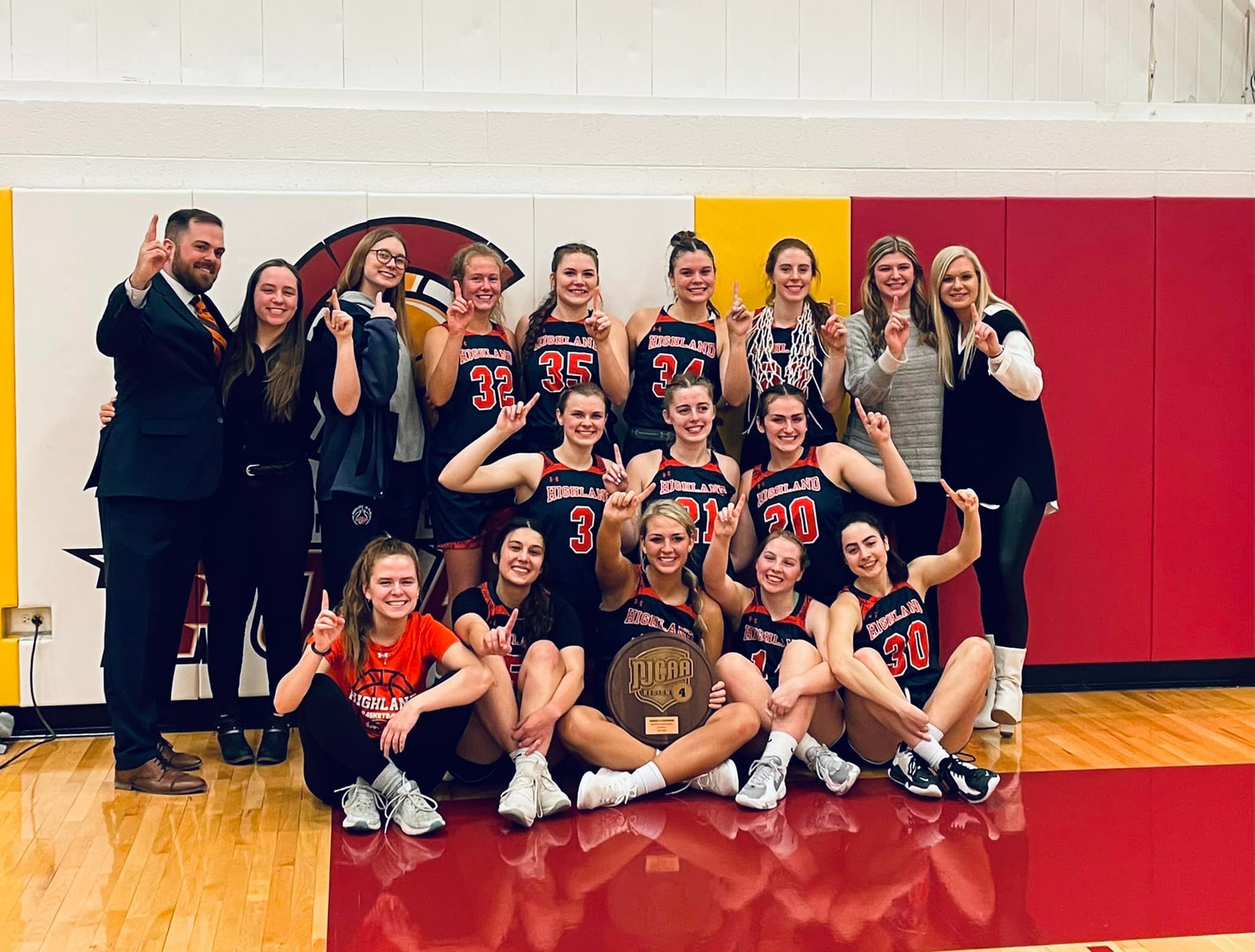Entire Women's Basketball Team and coaching staff with region IV Trophy holding up #1 on fingers