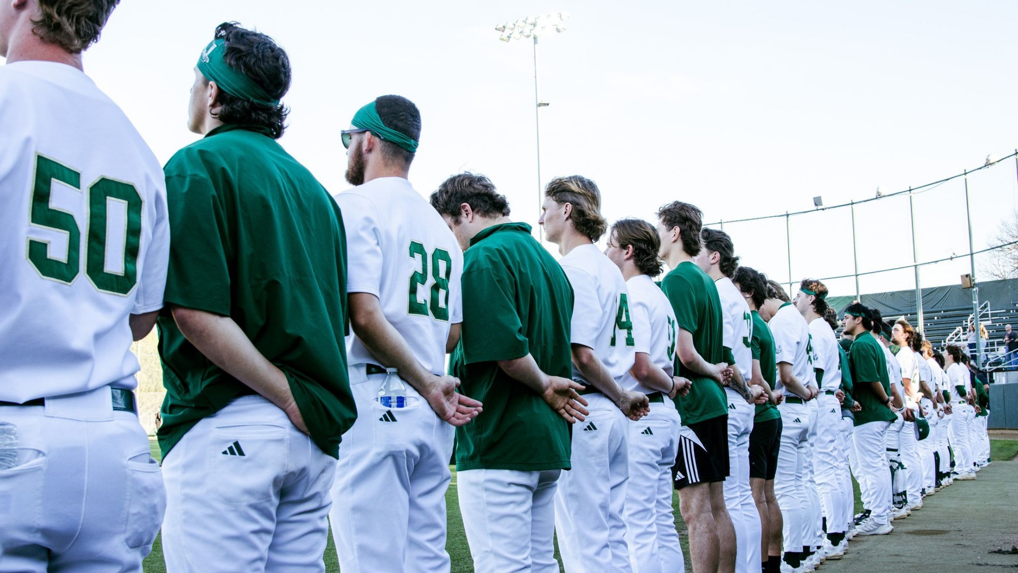 2026 BSB Hornet baseball players line up in front of the dugout for the national anthem prior to a game against Winthrop University