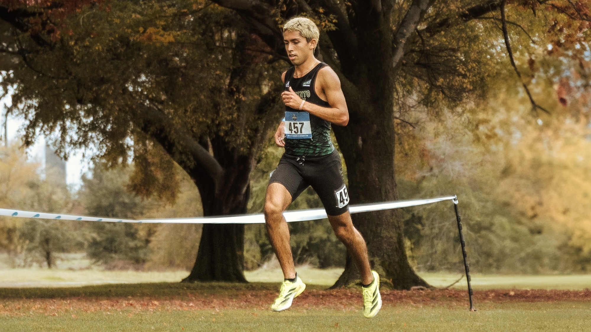 Photo of Ryan Martin running on a cross country course in front of a tree