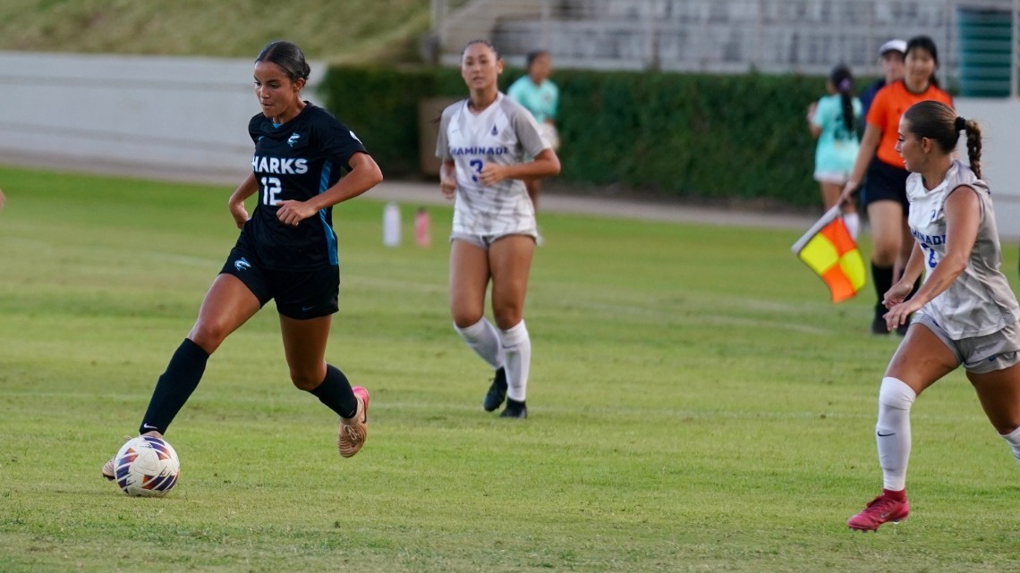                             Soccer players on the field, player on the left is dribbling the ball and wearing number 12 for HPU. 
