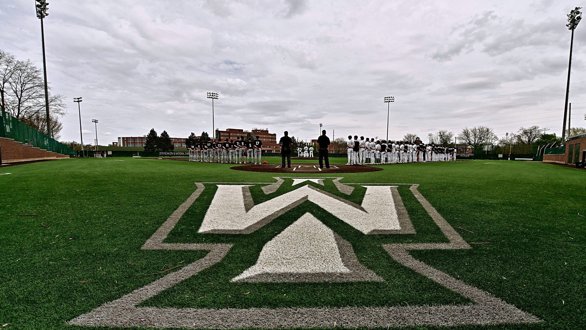 Illinois Wesleyan and Carthage line the baselines of Horenberger Field during the National Anthem