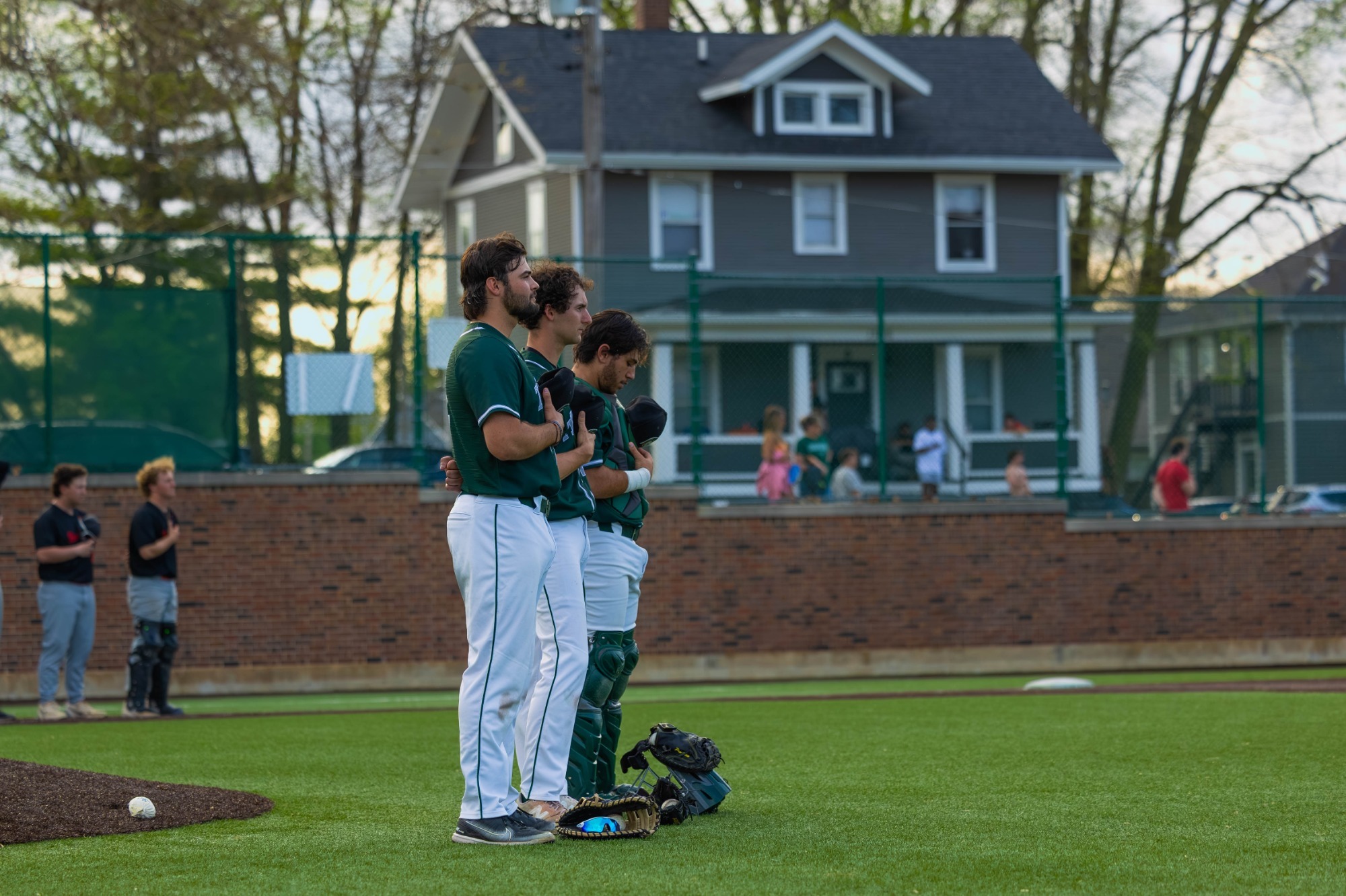 JP Ferraro, Jack Flagg, and Luca Morelli stand on the infield grass with their hands over their hearts during the playing of the national anthem