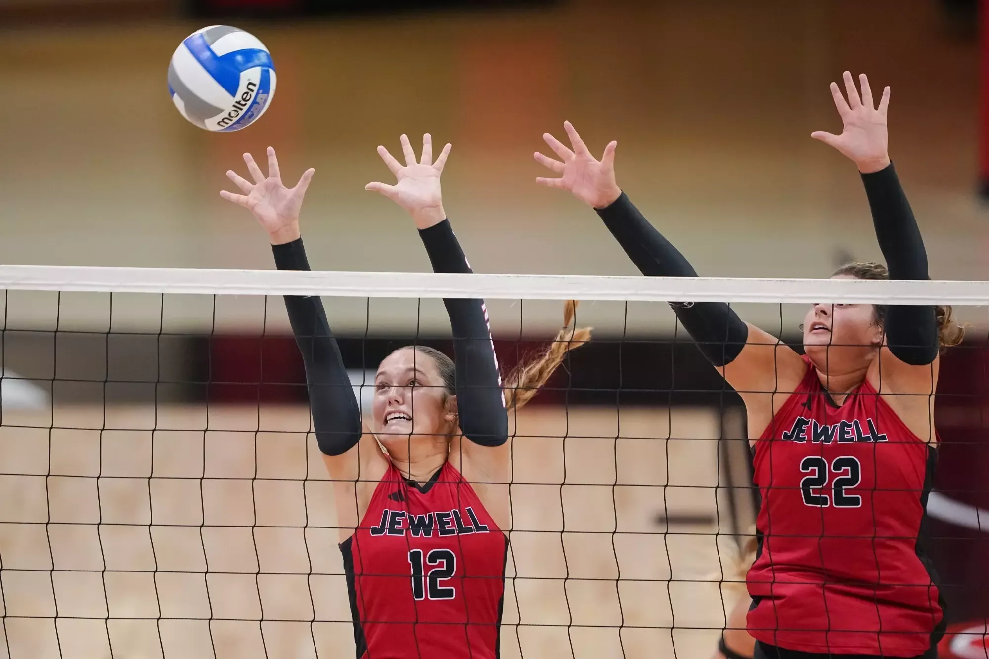 Silvia Fisher and Wylie Singleton jumping to block a volleyball with a net in front of them