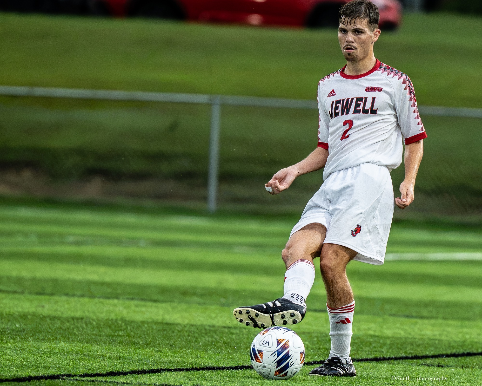 Miles Heckadon kick a soccer ball with his leg out, white Jewell soccer uniform 