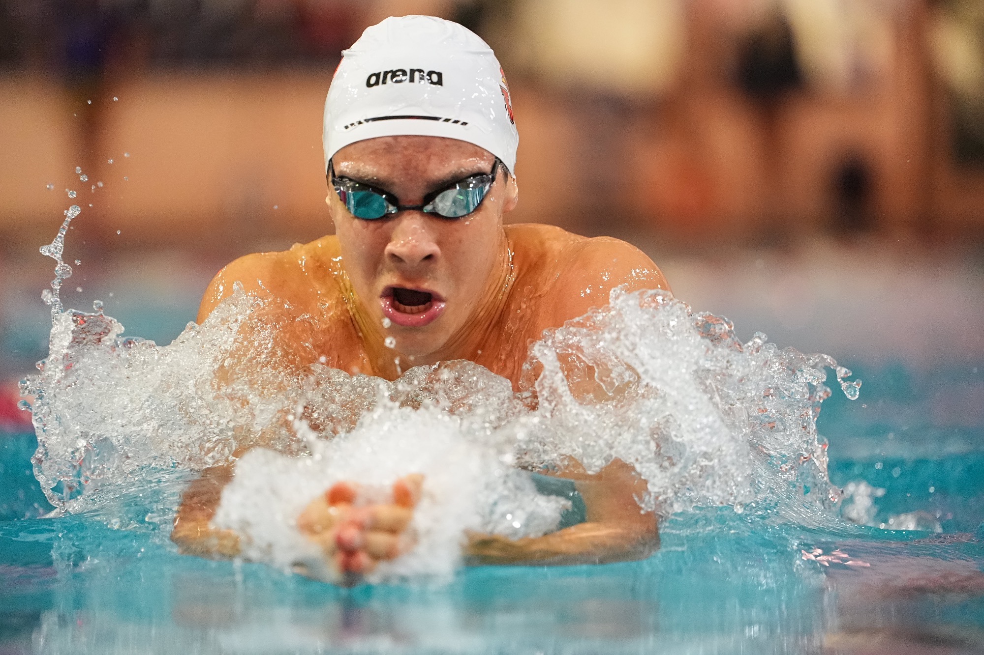 A swimmer comes out of the water with a white swim cap on in a very close up photo.