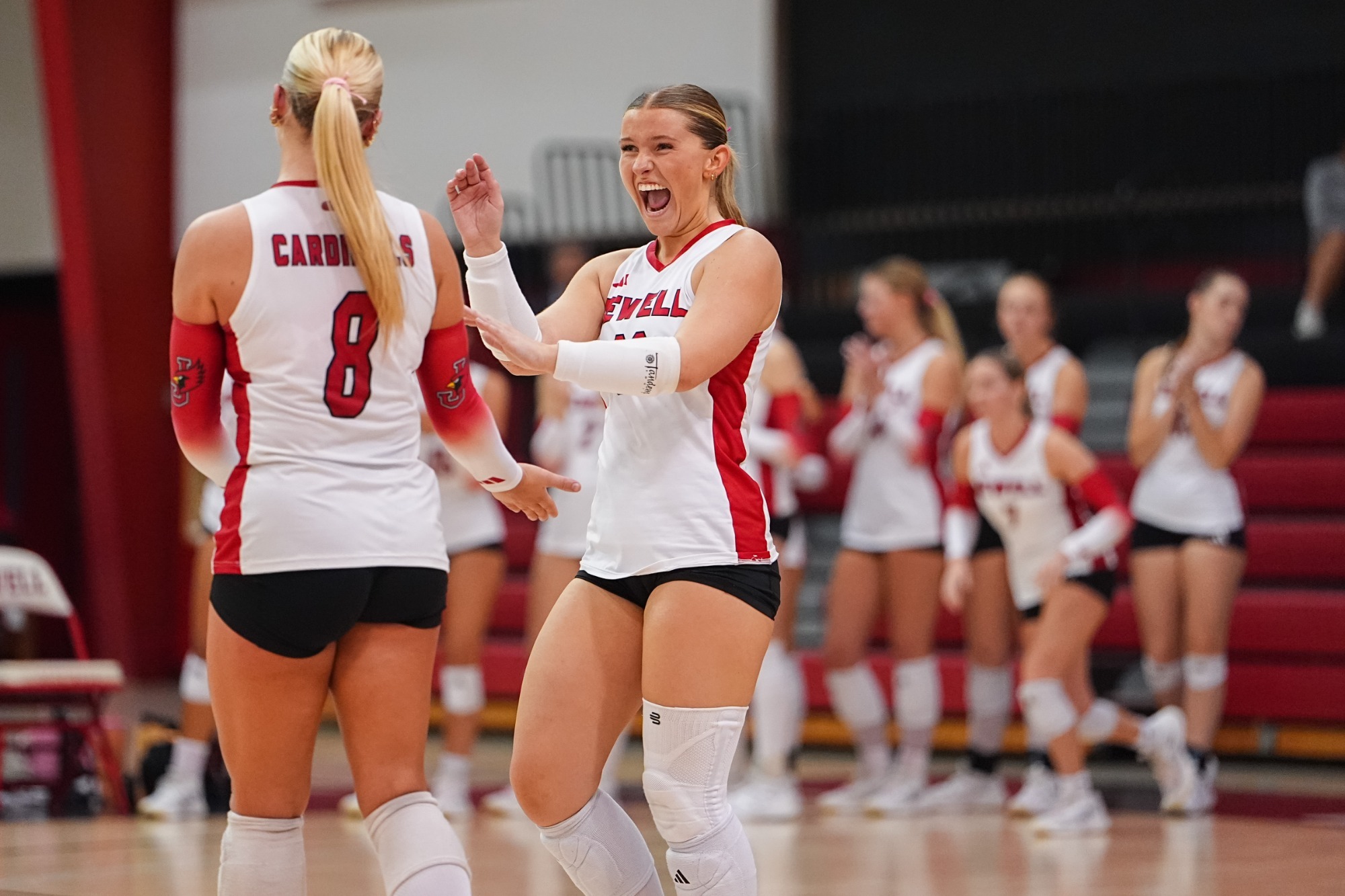 Madison Roney celebrates with Macy Bartlett as teammates applaud in the background during a volleyball match