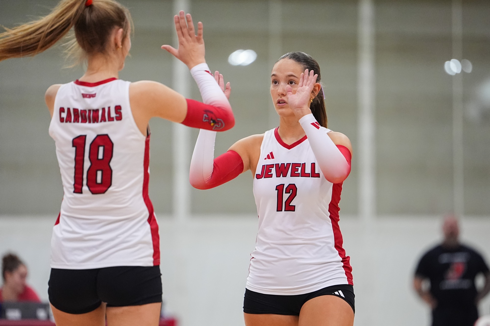 Silvia Fisher high fives Kali Adamec with two hands. Both players are wearing white Jewell volleyball jerseys