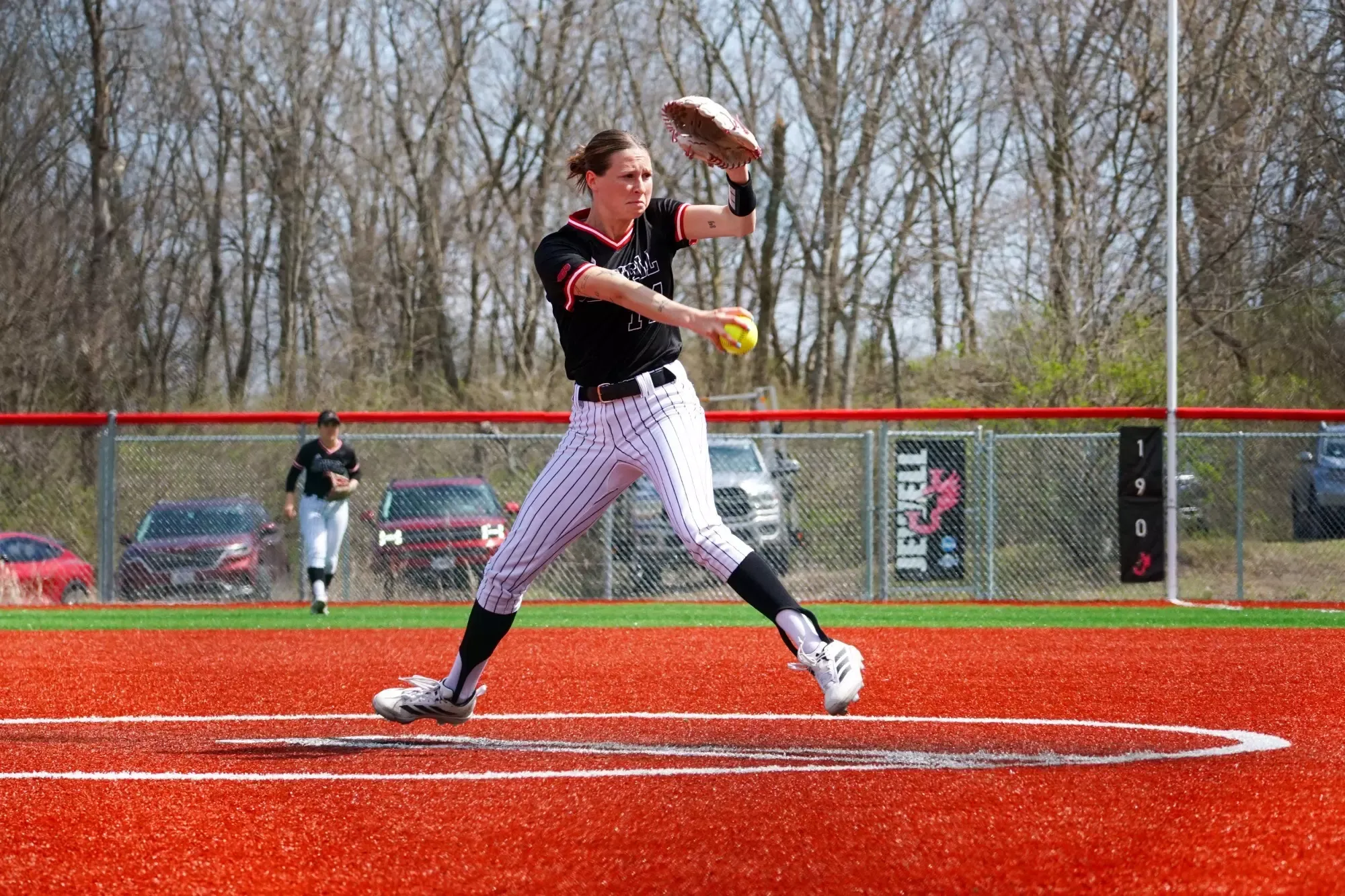 Softball player in pitching motion while wearing black uniform and striped pants