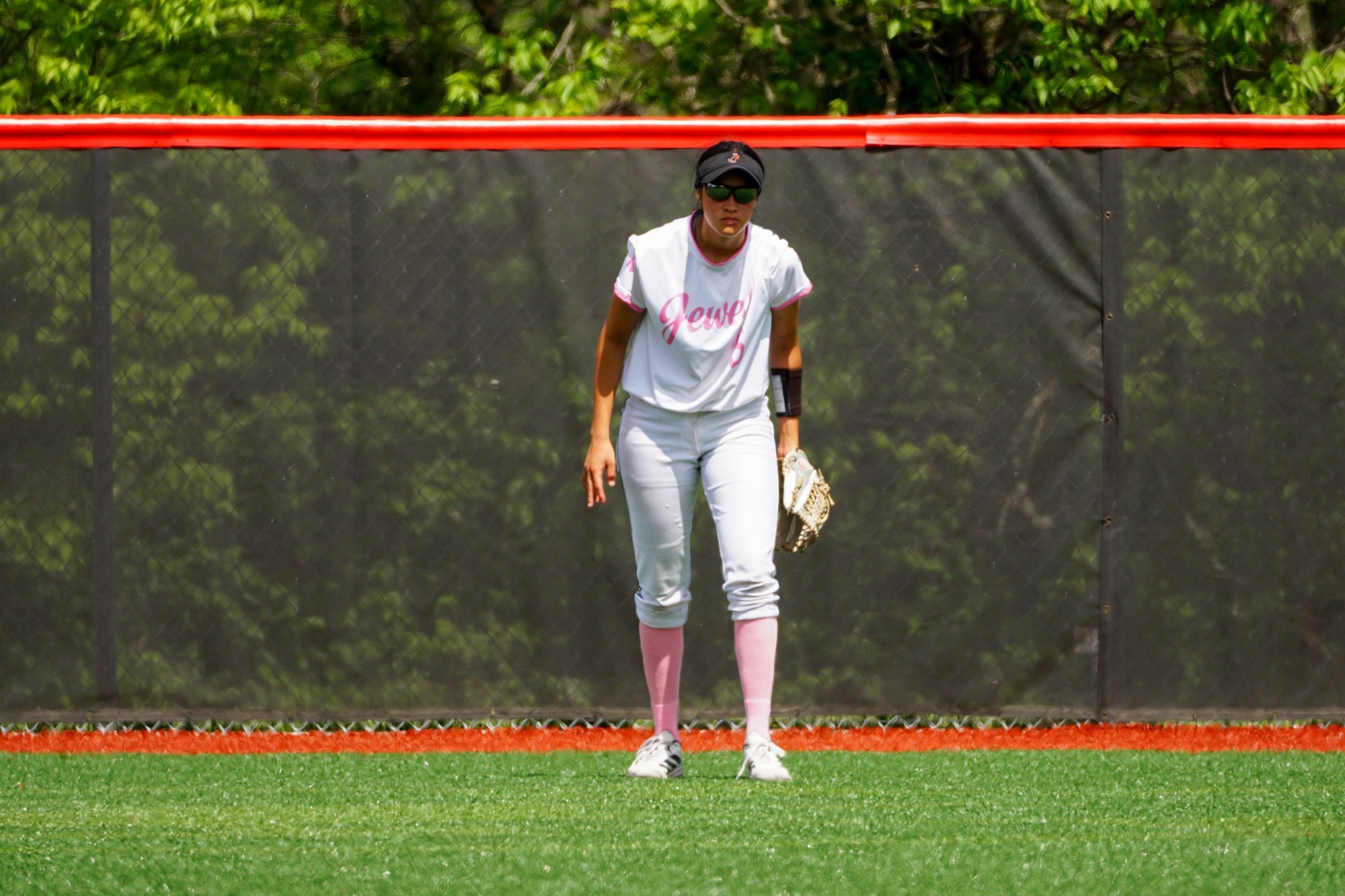 Softball player in white uniform standing in outfield