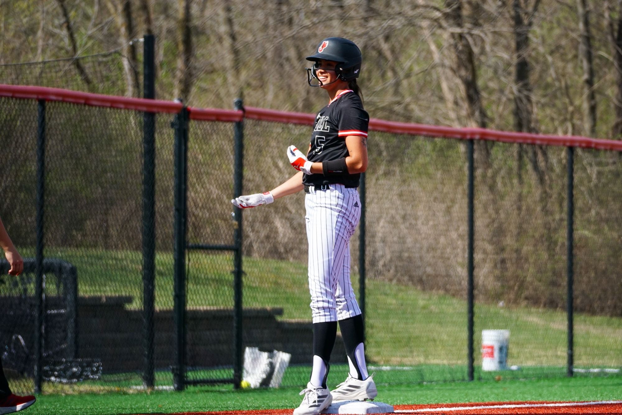 softball player in black top and white striped pants standing on third base