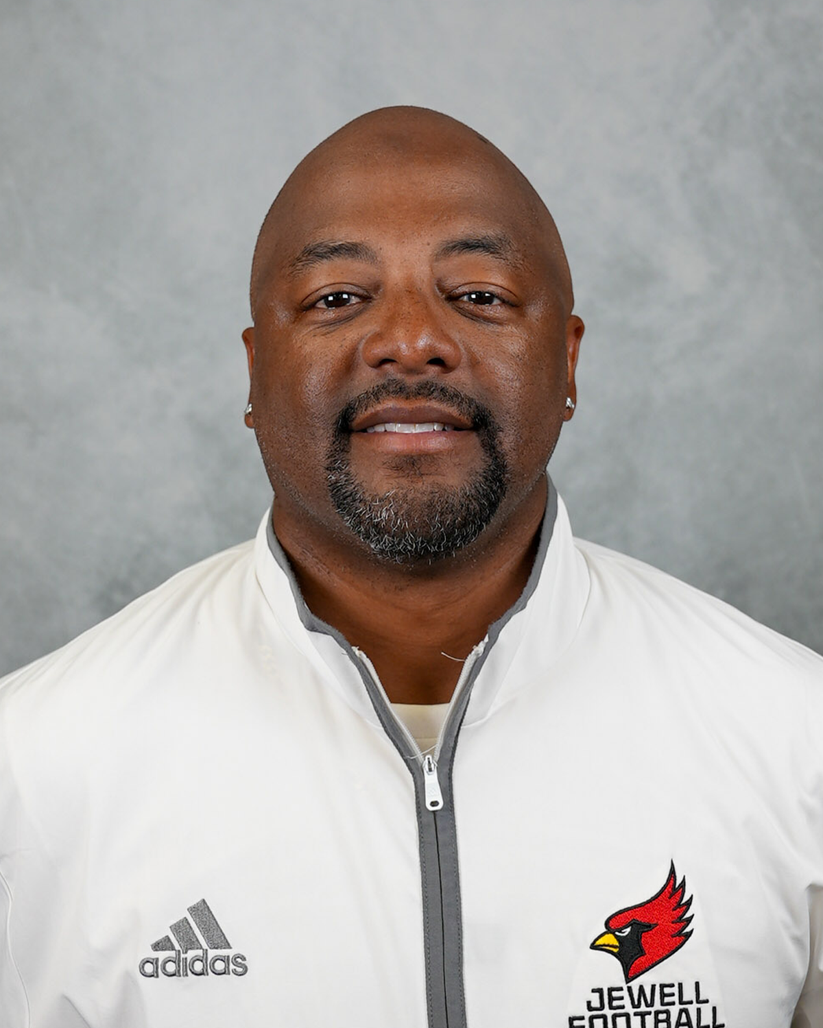 Headshot of William Jewell football coach Corey Bethany wearing a white Jewell Football pullover in front of a gray background