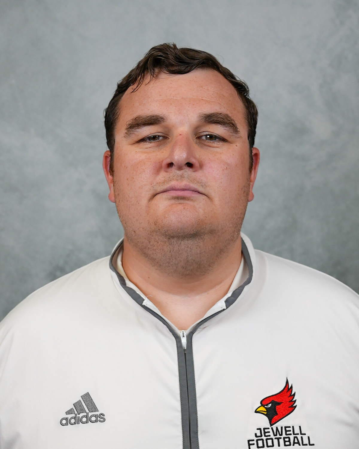Headshot of William Jewell football coach Jack Connelly wearing a white Jewell Football pullover in front of a gray background
