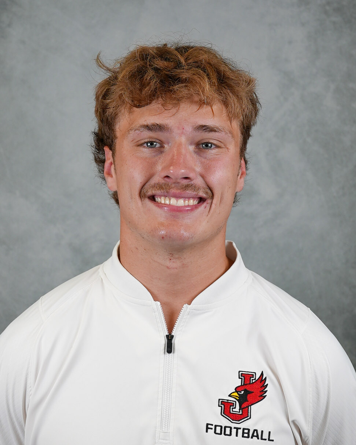 Headshot of William Jewell football coach Beau Doughty wearing a white Jewell Football pullover in front of a gray background