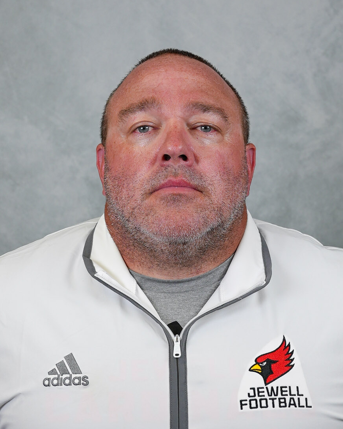 Headshot of William Jewell football coach Mark Faubion wearing a white Jewell Football pullover in front of a gray background