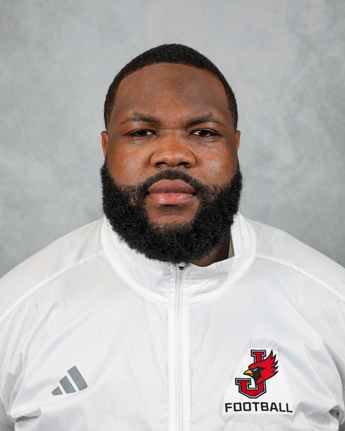 Headshot of William Jewell football coach Trey Hand wearing a white Jewell Football pullover in front of a gray background