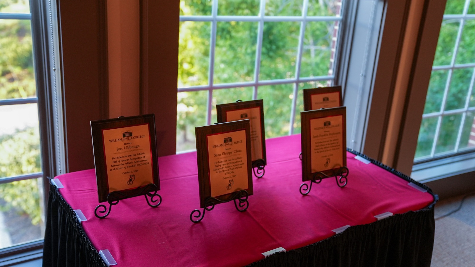 Image of five Hall of Fame plaques sitting in front of a window on a table with red and black cloth