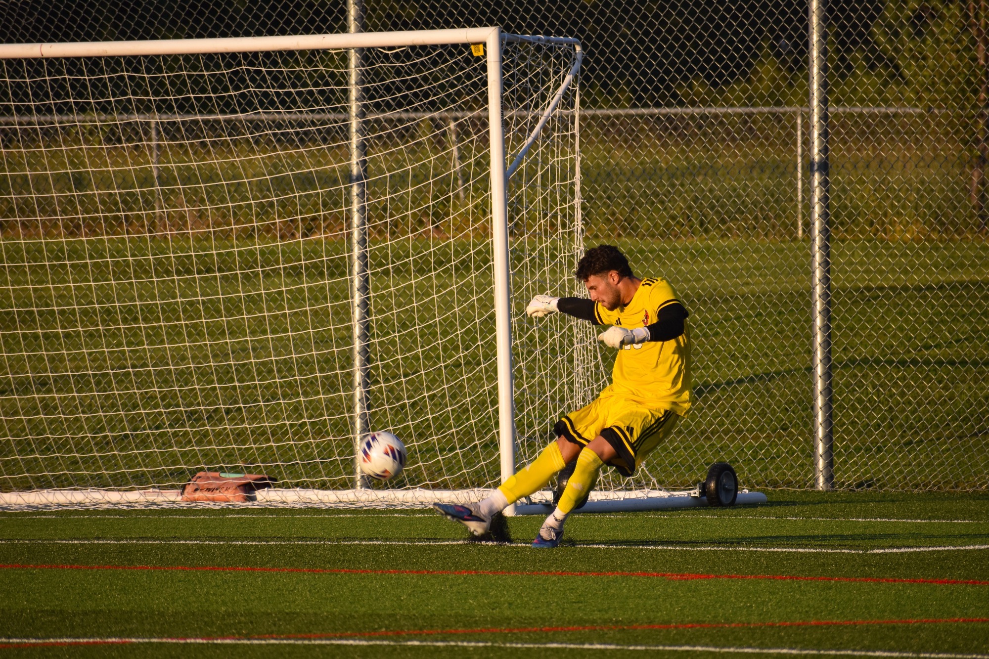 Alon Milwidsky in a yellow goalkeepers jersey kicking the soccer ball on a goal kick