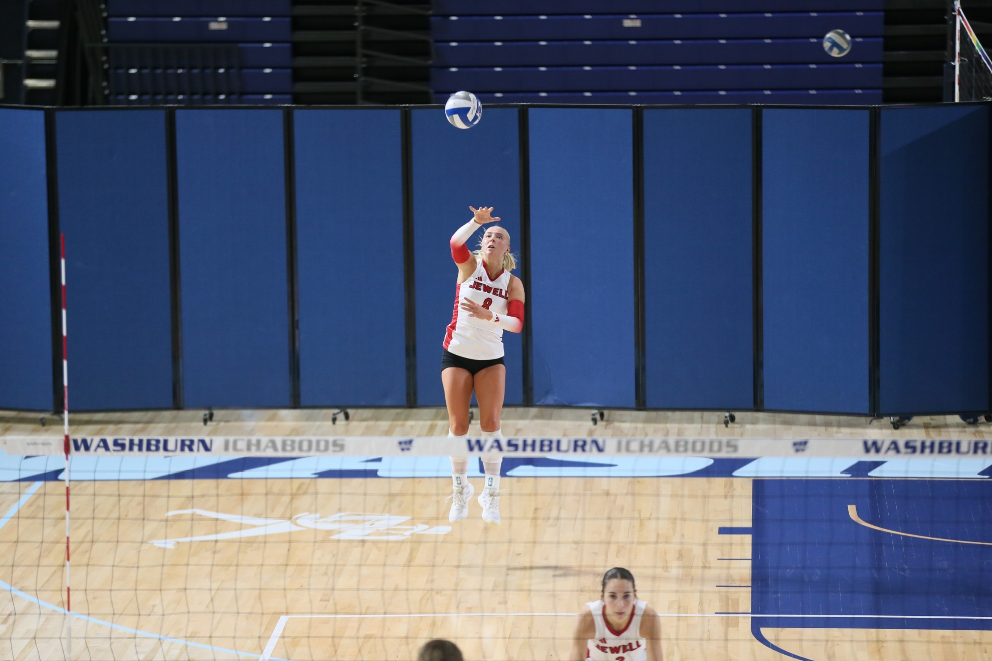 Macy Bartlett jumping for a serve, wearing a white jersey with a blurred net in the foreground
