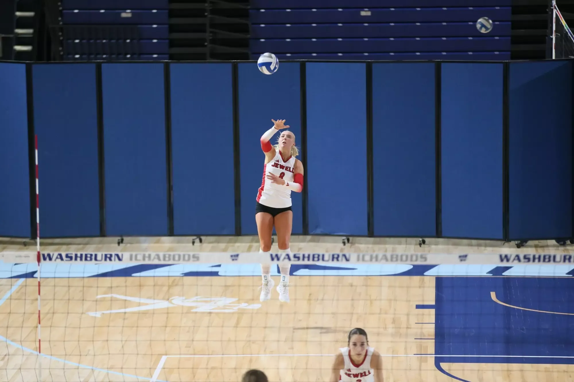 Macy Bartlett jumping for a serve, wearing a white jersey with a blurred net in the foreground