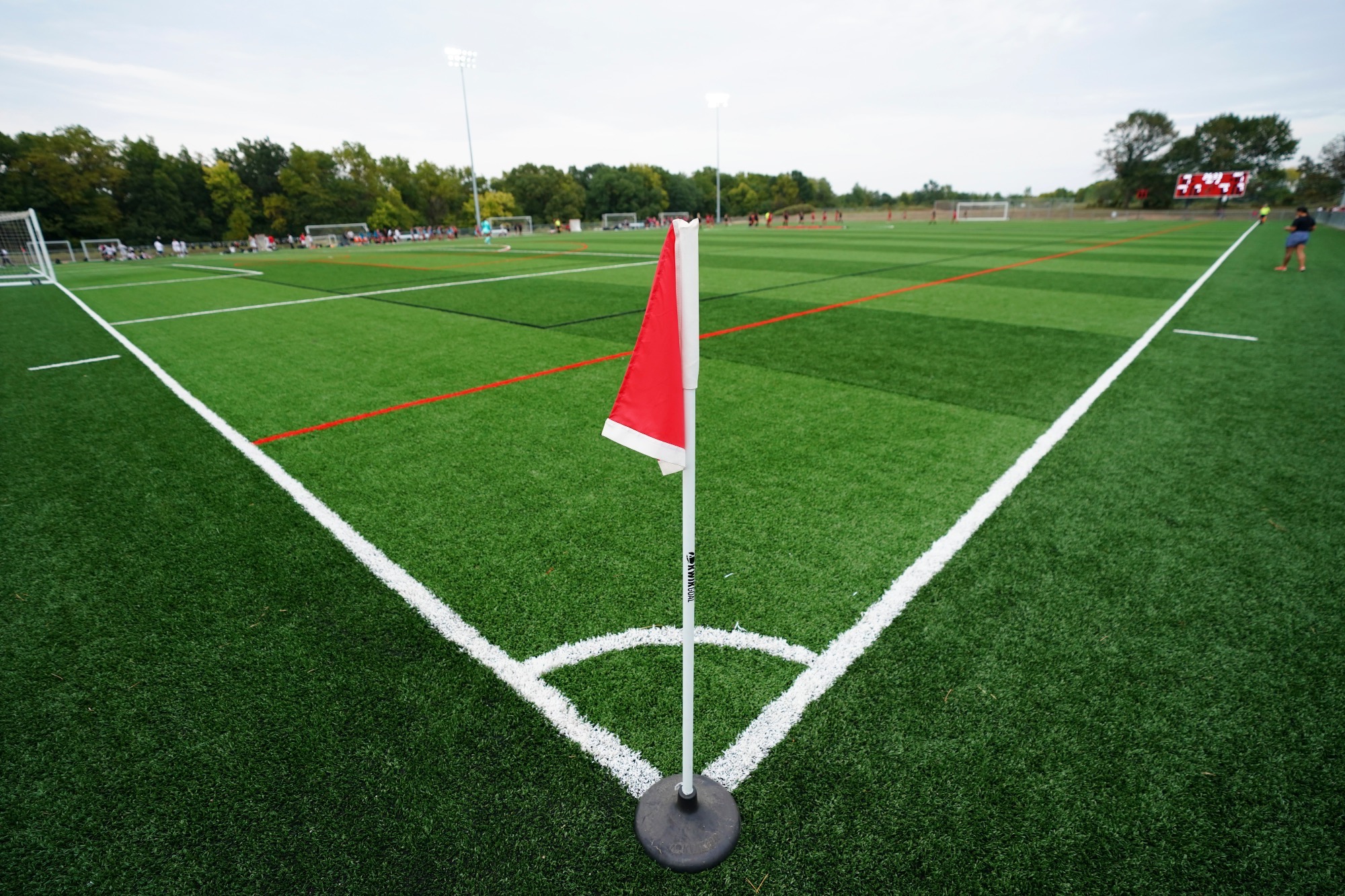A red flag on a white pole in the corner of a soccer field where the lines of the sideline and end-line meet