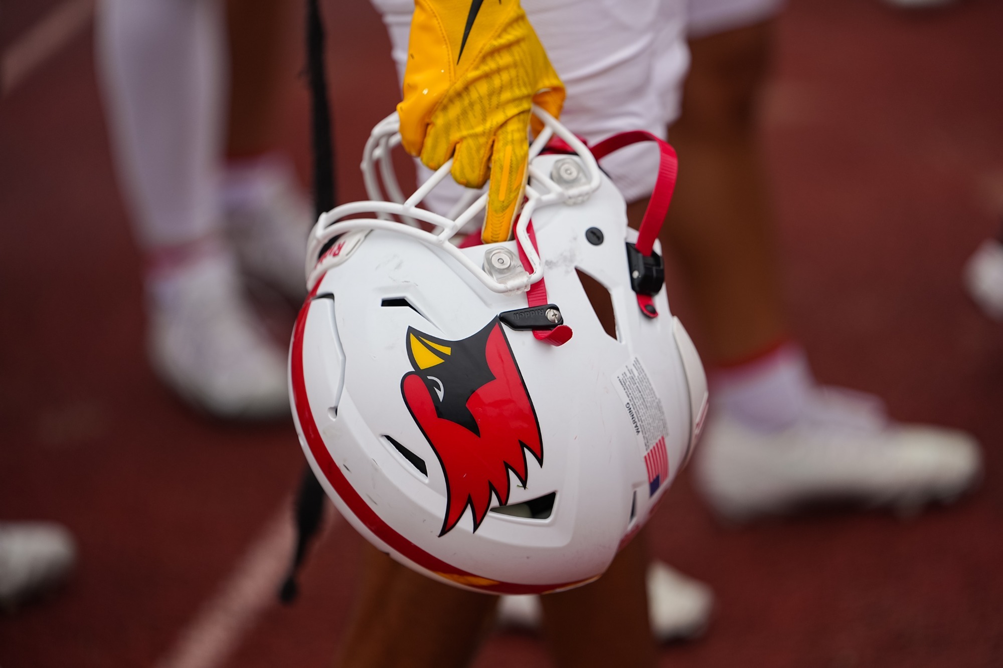 image of a football player held in a hand wearing a yellow glove with cleats visible and slightly blurred in the background