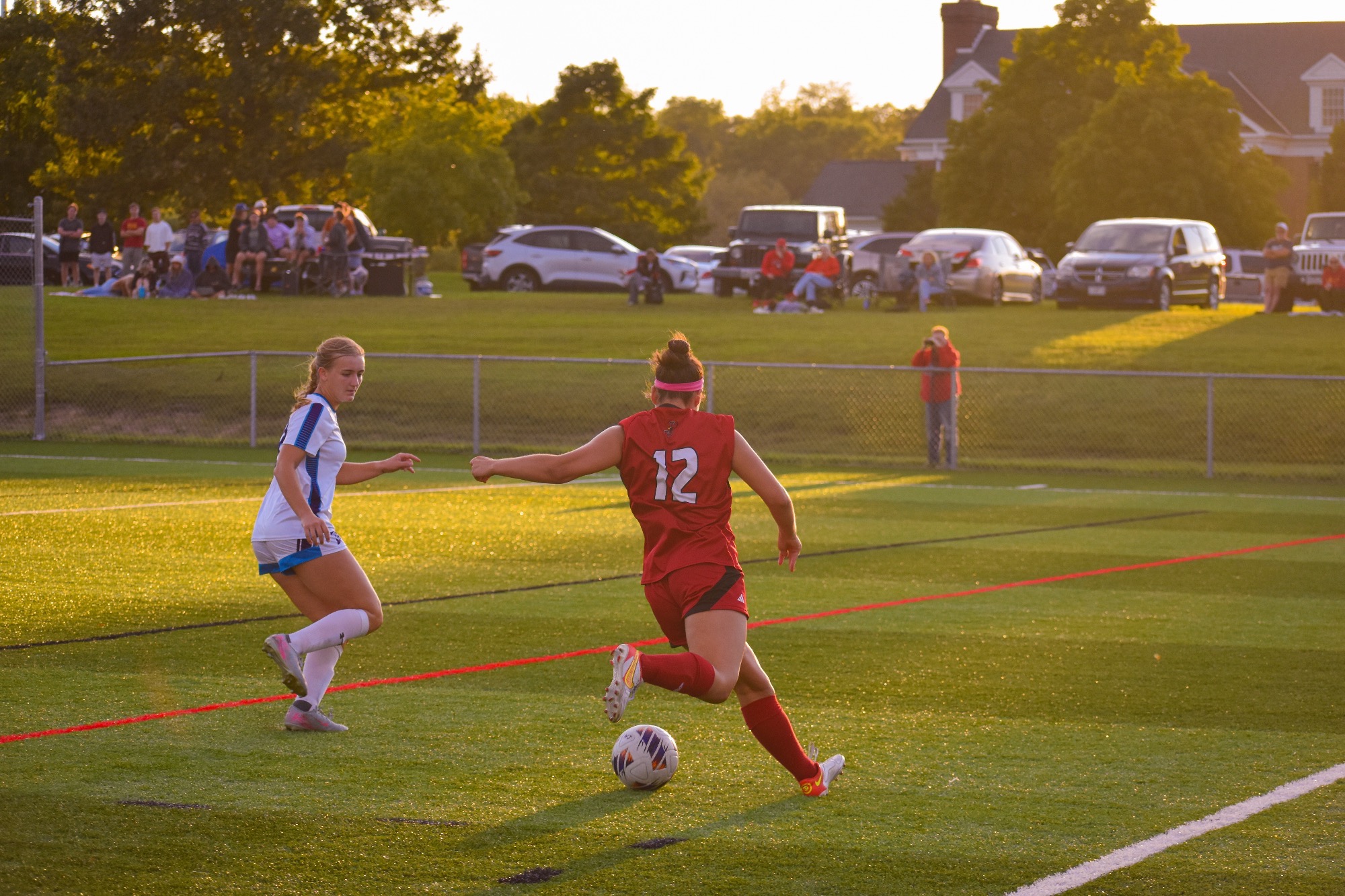 Elle Haan dribbles away a soccer ball in a red jersey with a white 12 on the back