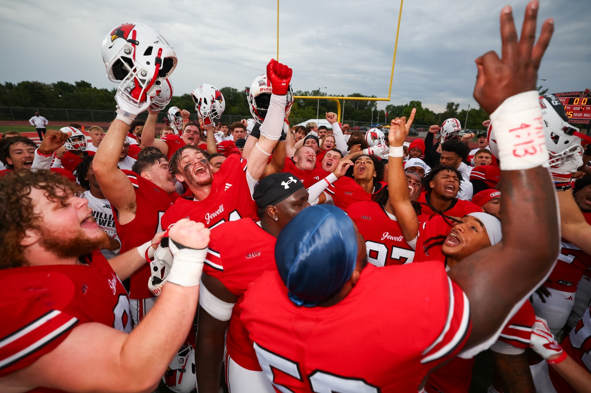 huddle of Jewell football players in red uniforms with fists raised in the air celebrating a win