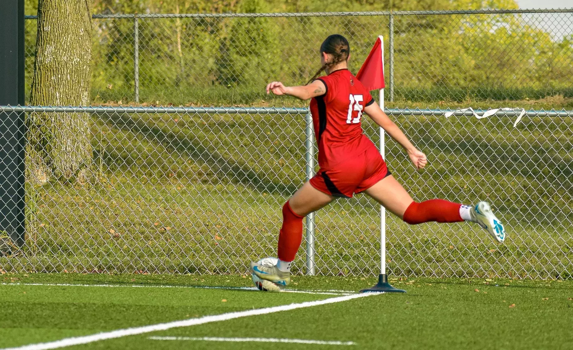 Dylin Davies kicks a soccer ball during a corner kick in red uniform