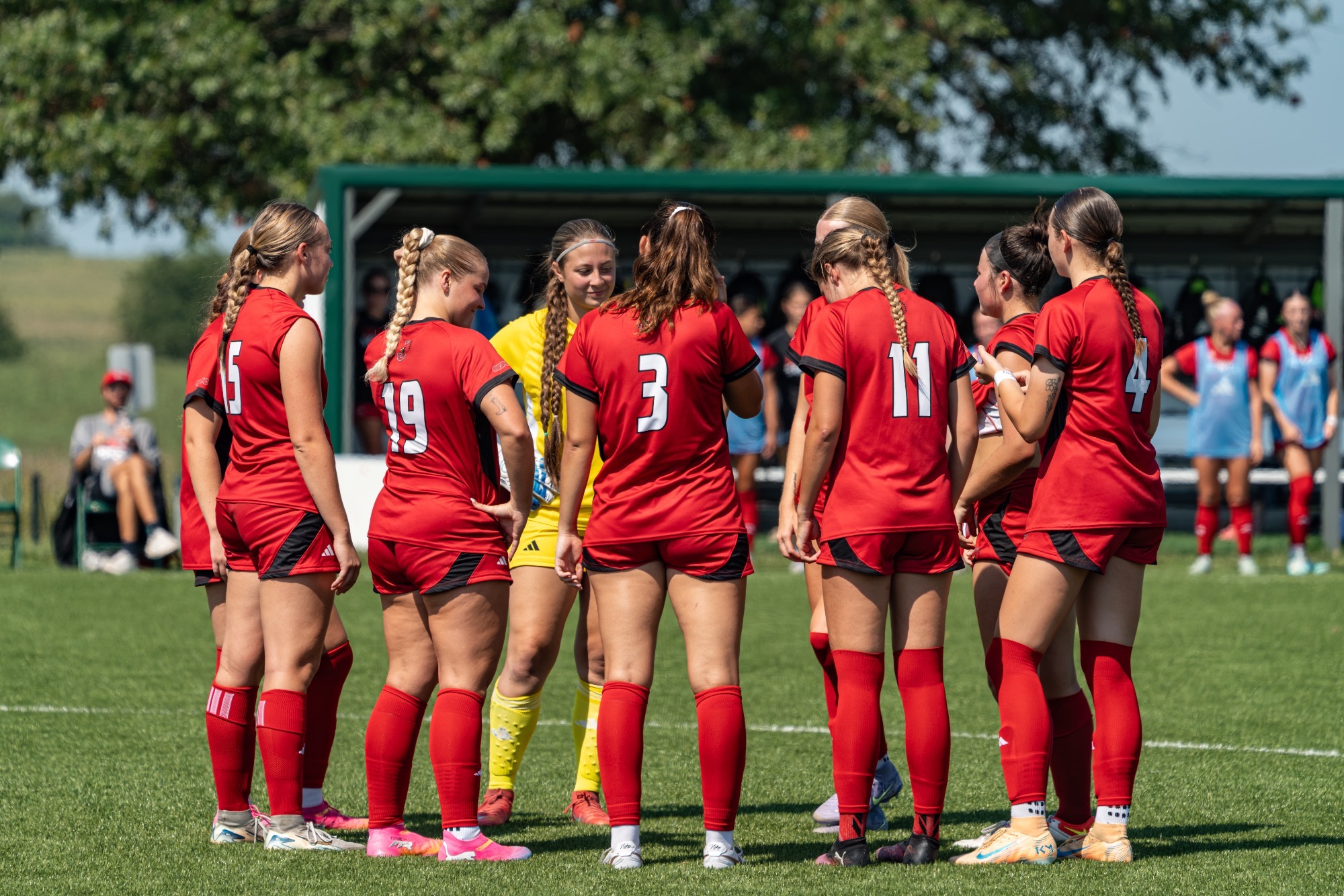 5 WSOC Players stand in a huddle wearing red jerseys 