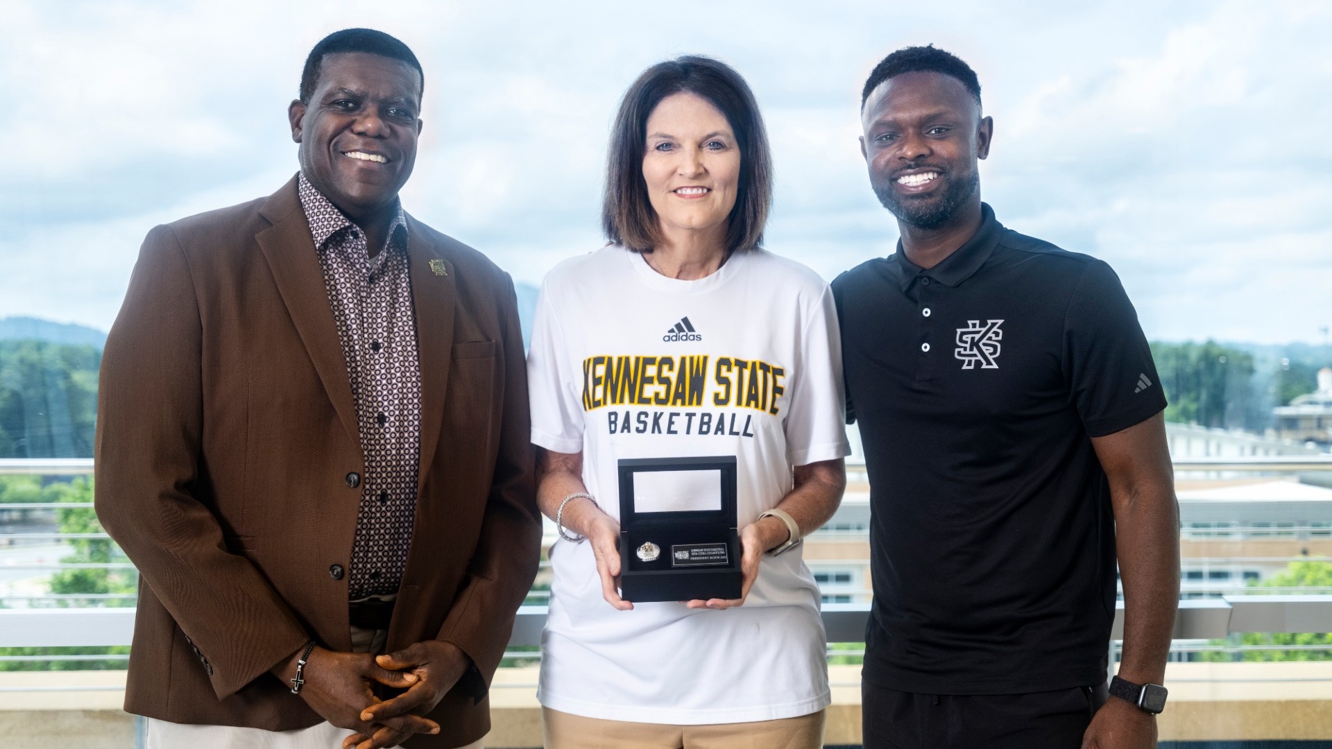 Kennesaw State men's basketball head coach Antoine Pettway and Director of Athletics Milton Overton present the 2026 CUSA Championship ring to university president Dr. Kathy Schwaig.
