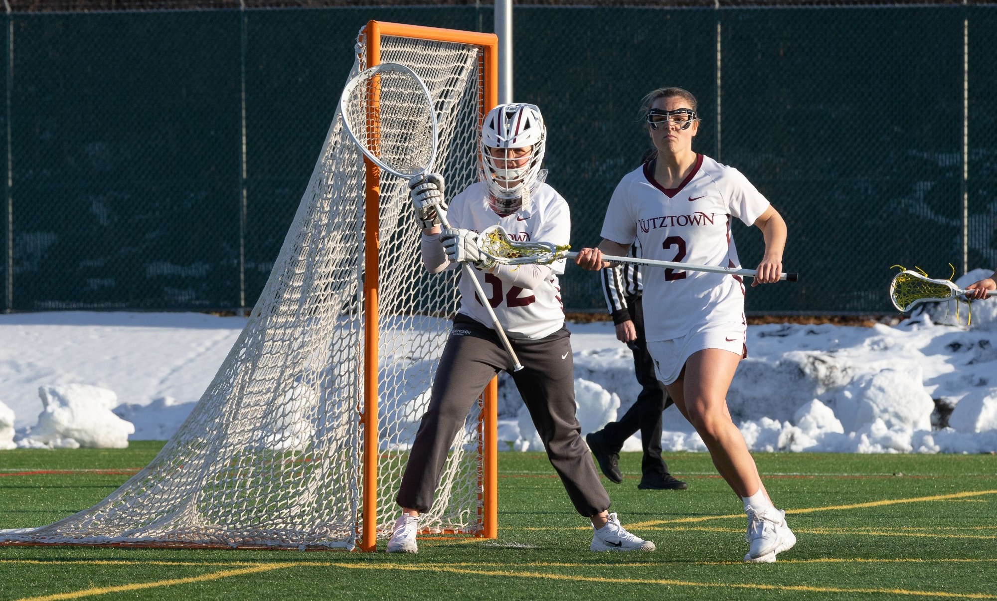 Marissa Brag stands in net, Summer Davis runs in front of cage