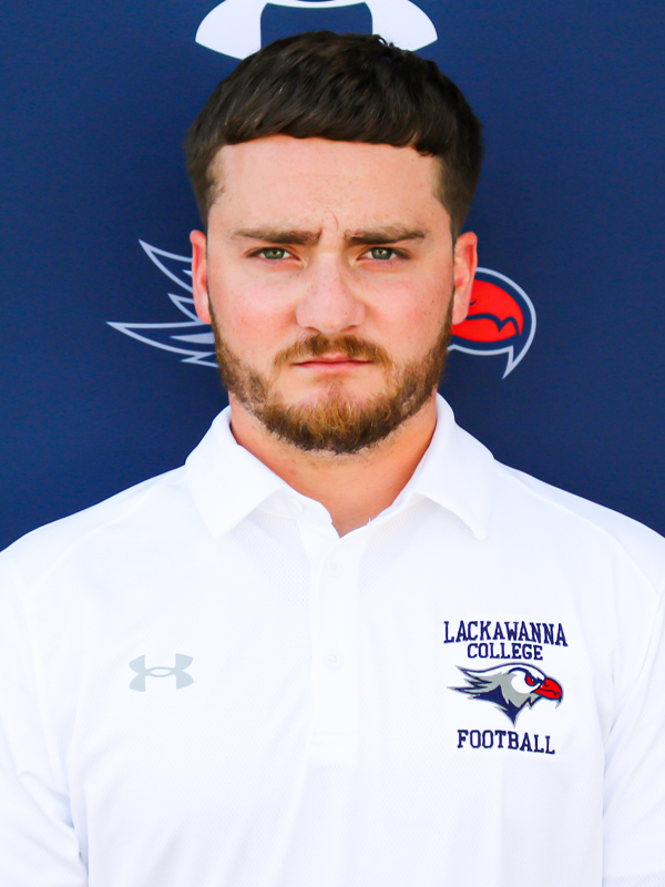 Assistant Football Coach Brandon Swingle In A White Shirt Standing In Front Of A Blue Lackawanna College Falcons Backdrop