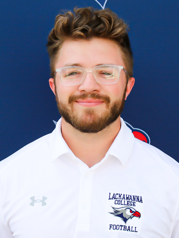 Assistant Football Coach Dayne Llamas In A White Shirt Standing In Front Of The Blue Lackawanna College Falcons Backdrop