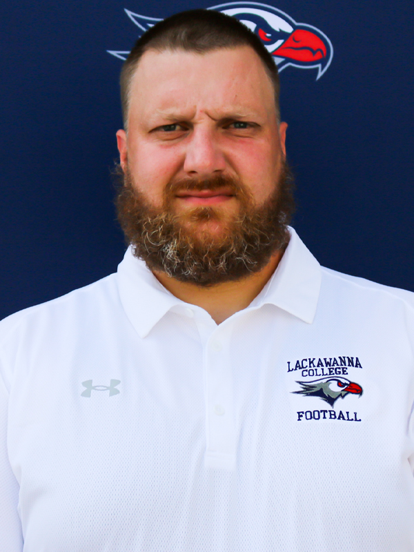 Assistant Football Coach Ray Dayton Standing In A White Shirt In Front Of The Blue Lackawanna College Falcons Backdrop