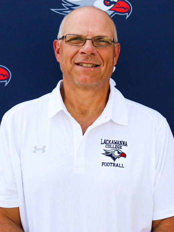 Head Football Coach Mark Duda In A White Shirt Standing In Front Of The Blue Lackawanna College Falcons Backdrop