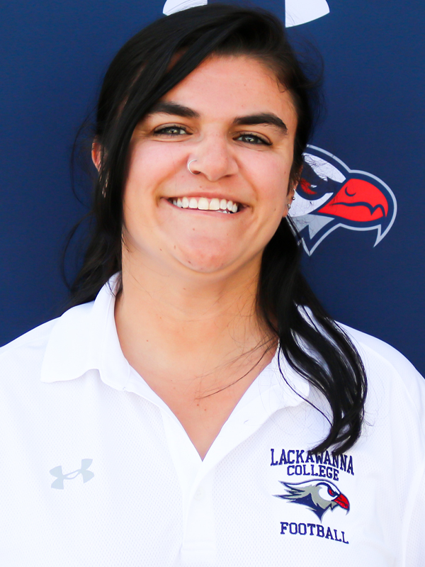 Athletic Trainer Katherine Godfrey In A White Shirt Standing In Front Of A Blue Lackawanna College Falcons Backdrop