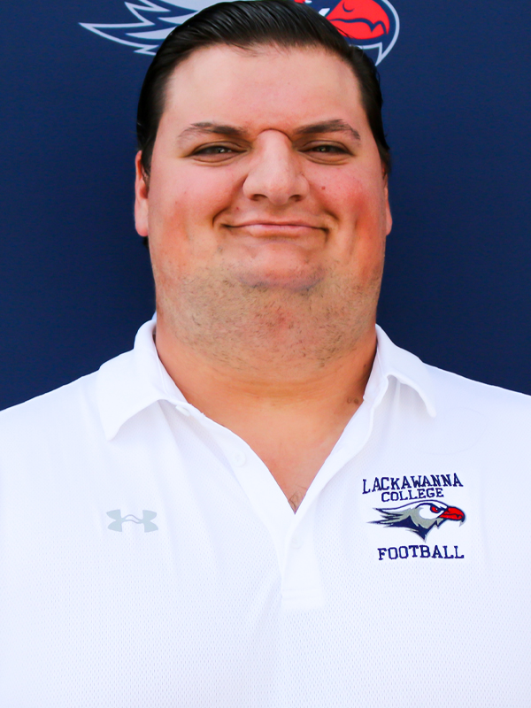 Trainer Ryan Natale In A White Shirt Standing In Front Of A Blue Lackawanna College Falcons Backdrop