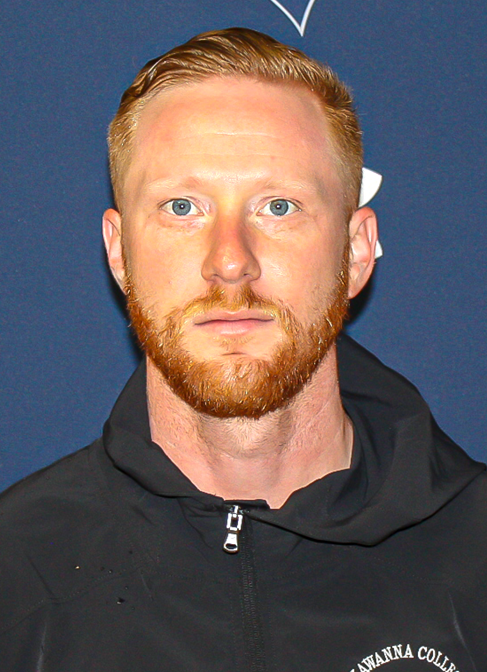 Assistant Soccer Coach Brendon Weinhardt Standing In Front Of A Blue Background With The Lackawanna College Logo On It