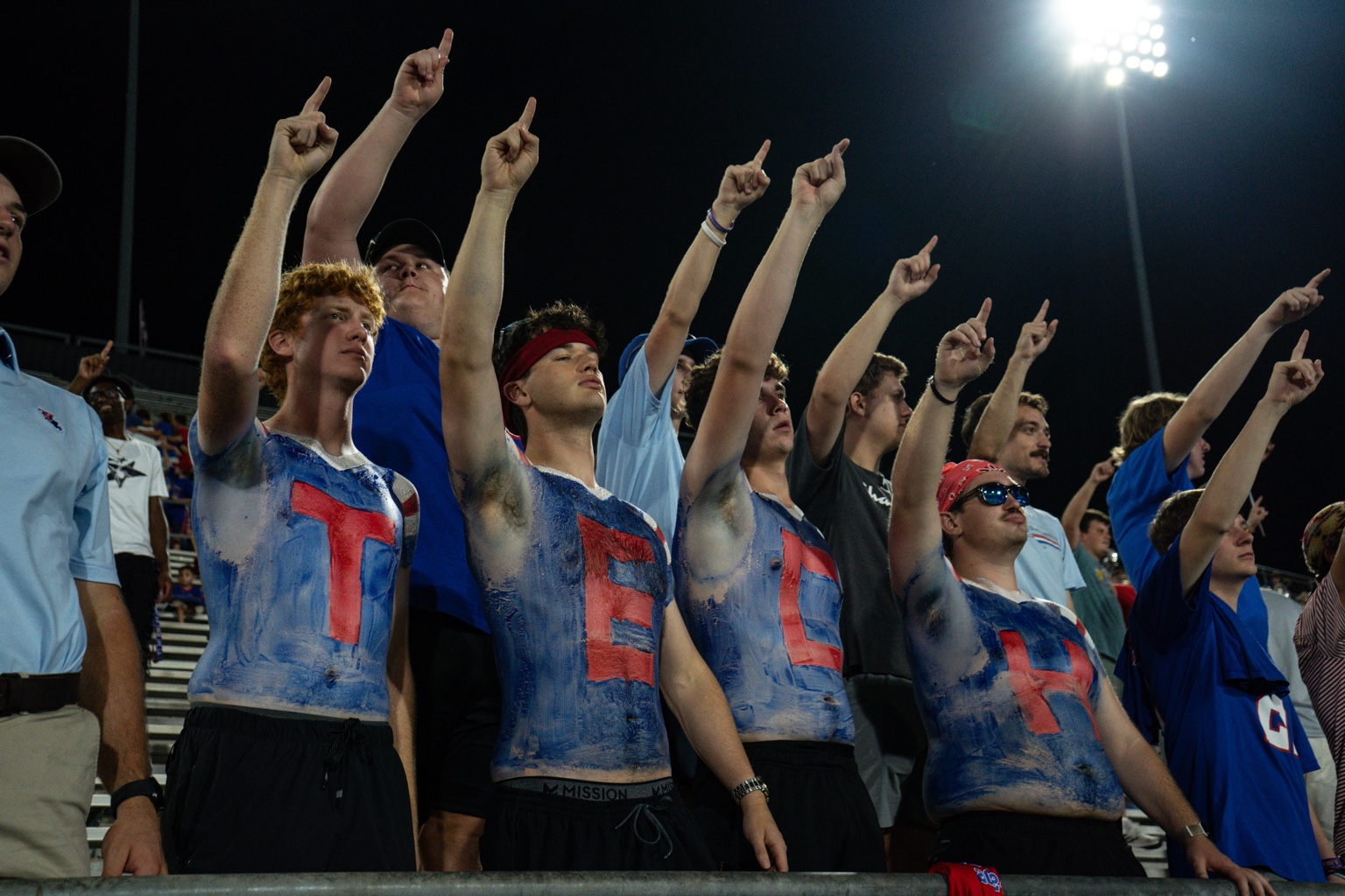 LA Tech football students with painted chests pointing under the lights