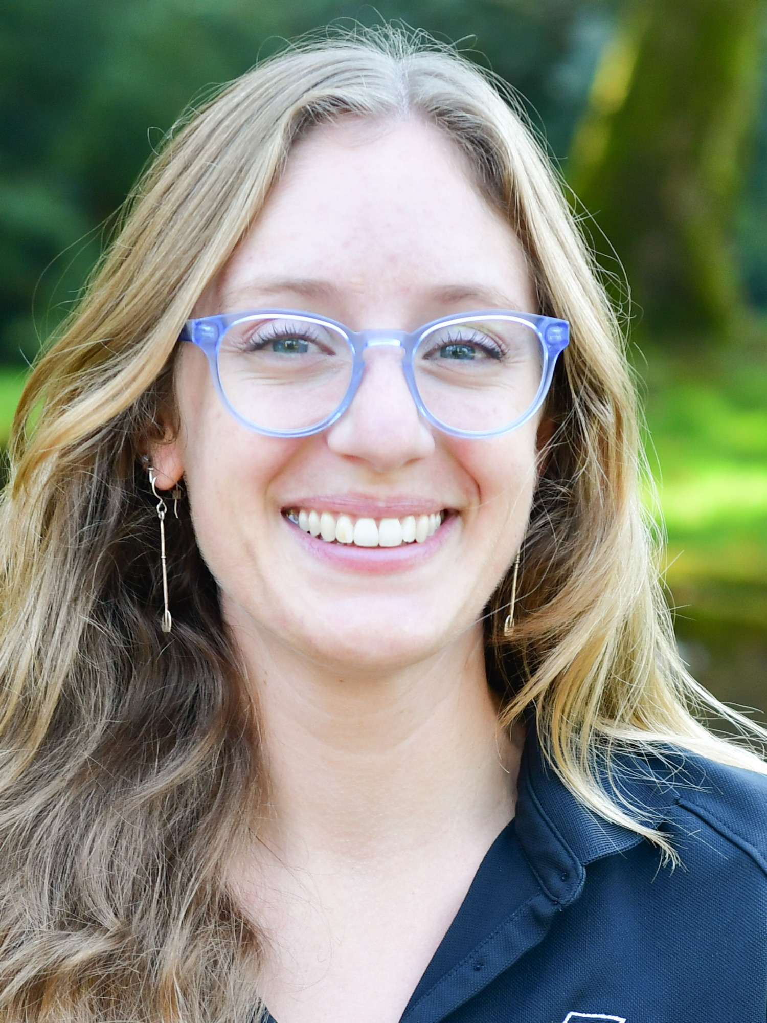 Claudia Loeber stands outside in front of a green background, smiling.
