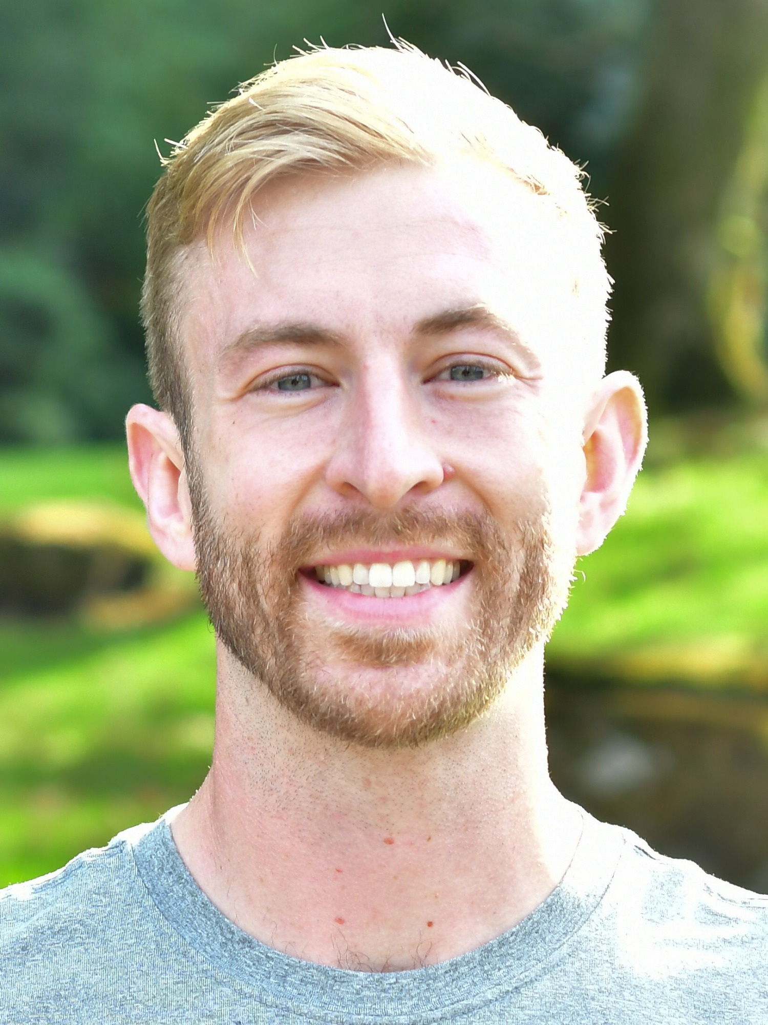 Kyle Dreibelbis stands outside in front of a green background, smiling.