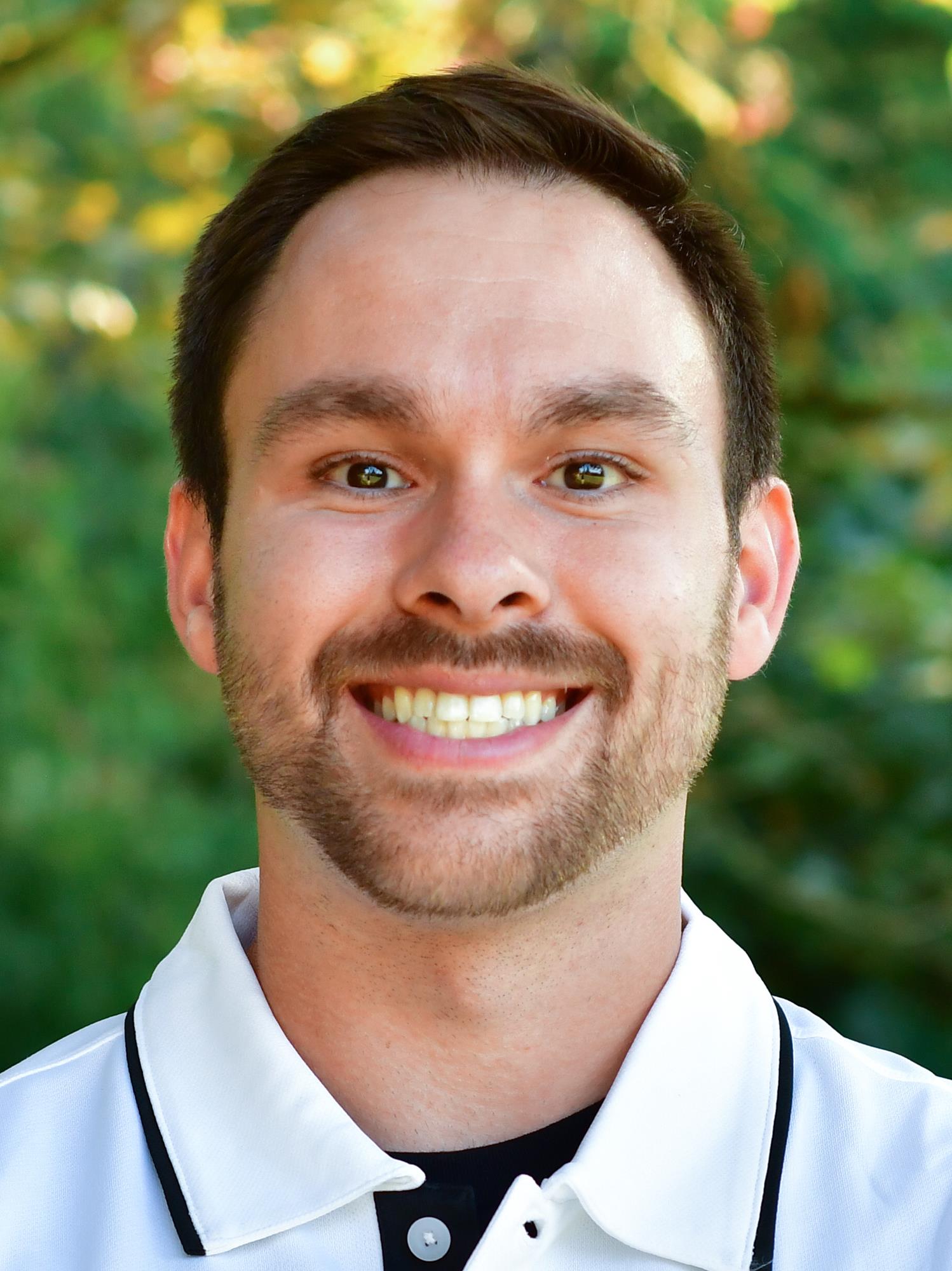Matt Mayberg stands outside in front of a green background, smiling.