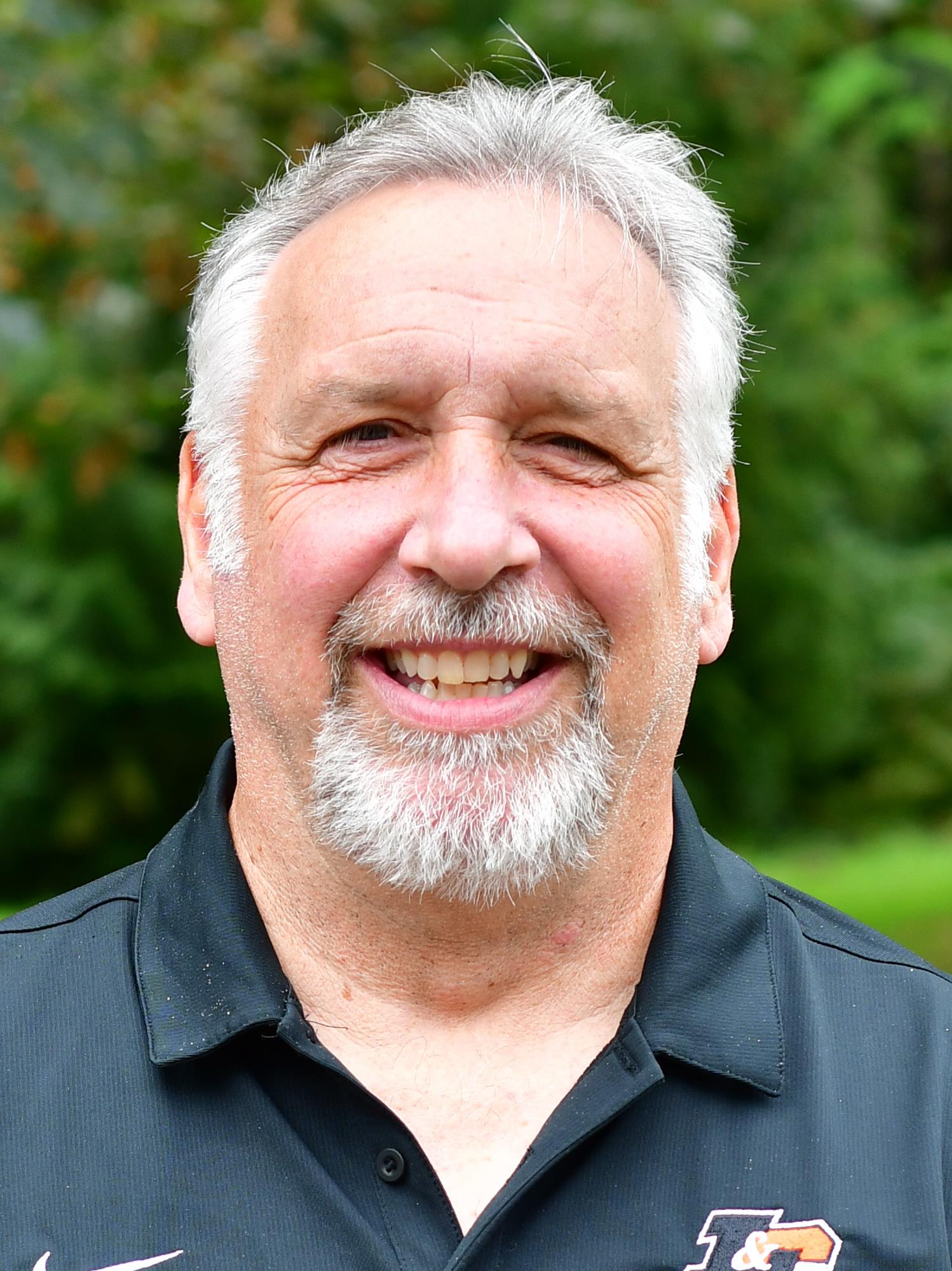 Jim Tursi standing outside in front of a green background, smiling.