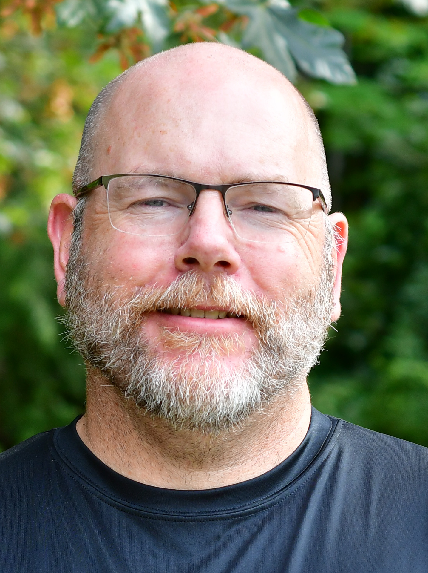Patrick Rockenbaugh standing outside in front of a green background, smiling.